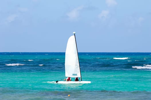 A sailboat is sailing on the blue caribbean sea.