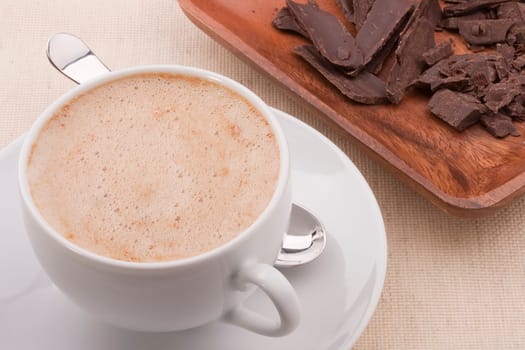Cappuccino in a white ceramic cup with a saucer and a spoon.