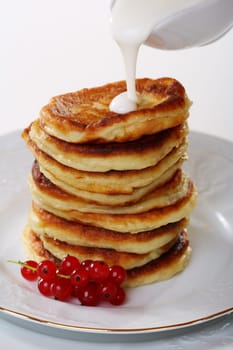 Pancakes with sour cream sauce and red currants on a white background.