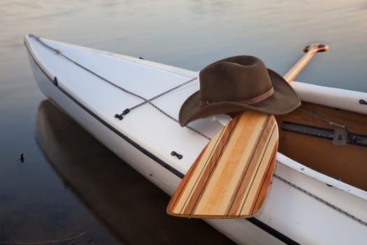 a cowboy hat,a wooden paddle across cockpit of decked expedition canoe
