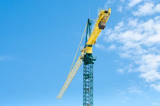 yellow with green crane against a partly clouded blue sky