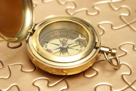 A brass compass rest on top of a golden jigsaw puzzle for different concepts.