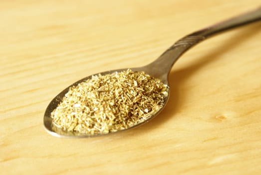 A teaspoon full of Chamomile tea over a wooden background.