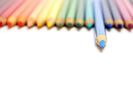 A spectrum of colored pencil crayons with a blue one ahead of the rest with a shallow depth of focus.