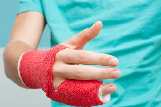 Injured male hand with upper part of body. Hand is bandaged with red plaster focus set on thumb