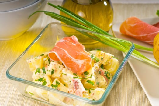 fresh home made parma ham and potato salad,with raw ingredients around with bowls and dishware on a table