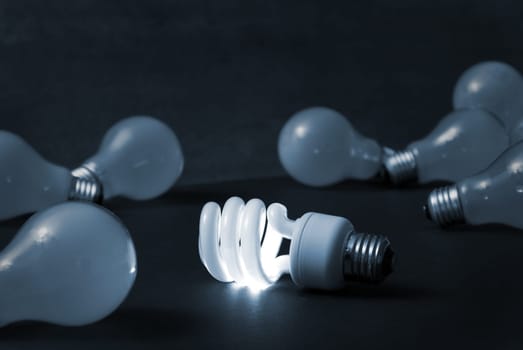 A new energy efficient CFL light bulb shines while the old ones fade into darkness.