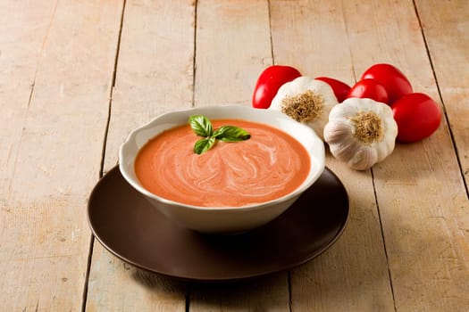 photo of delicious tomato cream soup on wooden table with garlic and basil