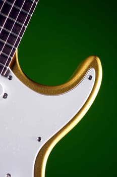 An electric metallic gold guitar close up isolated against a green background in the vertical format.