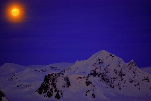 Moon on the dark blue sky among mountains. Antarctica.