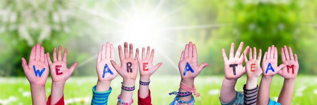 Children Hands Building Colorful English Word We Are A Team. Summer, Sunny Green Grass Meadow As Background