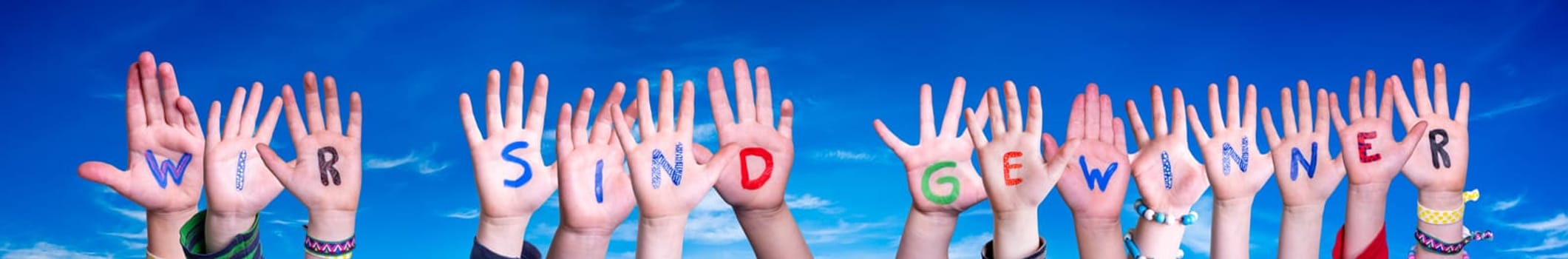 Children Hands Building Colorful German Word Wir Sind Gewinner Means We Are Winners. Blue Sky As Background