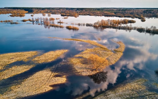 Spring flood rural landscape. Trees, meadow, bushes, fields, country road under High Water inundation. Sky, clouds reflection in evening light. Freshet Overflow aerial view. Floodplain area. Belarus