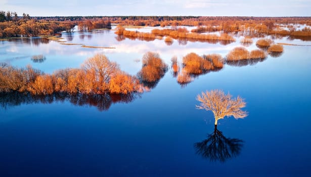 Spring flood rural landscape. Trees, meadow, bushes, fields, country road under High Water inundation. Sky, clouds reflection in evening light. Freshet Overflow aerial view. Floodplain area. Belarus
