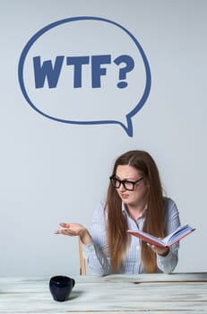 Young perturbed businesswoman with glasses and notebook looking away on light gray background. at the top of the photo the inscription WTF