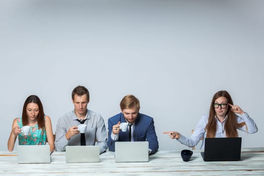 Business team working together at office on light gray background. boss is dissatisfied with the others drinking tea. copyspace image