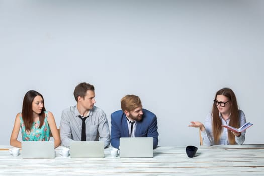 Business team working together at office on light gray background. all working on laptops. boss reading notebook. copyspace image