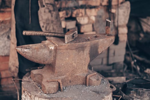 Process metal with hammer on anvil in forge. Strike iron outdoors in workshop with fire. Metalworking, blacksmithing, manufacturing equipment and tools. Traditional technic of making hardware.