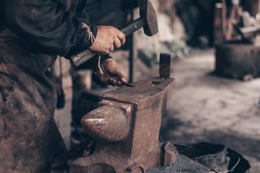 Blacksmith process metal with hammer on anvil in forge. Farrier in dirty clothes strike iron in workshop. Metalworking, manufacturing equipment and tools. Traditional technic of making hardware.