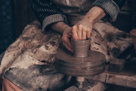 Modeling bowl from clay on wheel in pottery workshop. Dirty hands of craftsman mold crockery. Technique of crafting clayware. Working on potter wheel with raw clay, shaping pot. Traditional crafting.