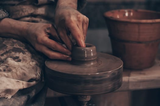 Modeling bowl from clay on wheel in pottery workshop. Dirty hands of craftsman mold crockery. Technique of crafting clayware. Working on potter wheel with raw clay, shaping pot. Traditional crafting.