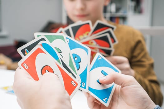 Belarus, Minsk, 08.01.2023. Boys play UNO. Hands of children hold paper colorful cards with numbers in fan closeup. Interesting card game. Home leisure, playtime. Board game for kids.