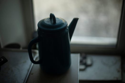 Kettle on background of window. Kettle with handle. Silhouette of kitchen utensils. Kitchen details.