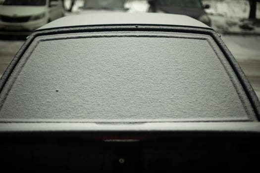 Rear window of car in snow. Snow by car. Car is parked in winter. Snow on glass.