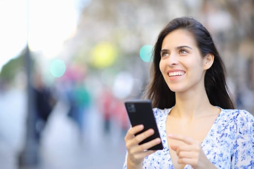 Happy woman holding cell phone looks up in the street