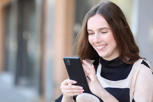 Happy elegant woman using cell phone standing in the street