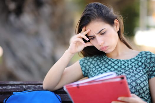 Frustrated student trying to learn sititng on a bench in a park