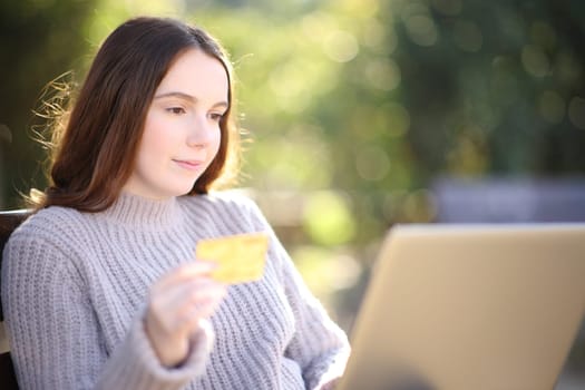 Serious woman buying with credit card and laptop sititng in a park