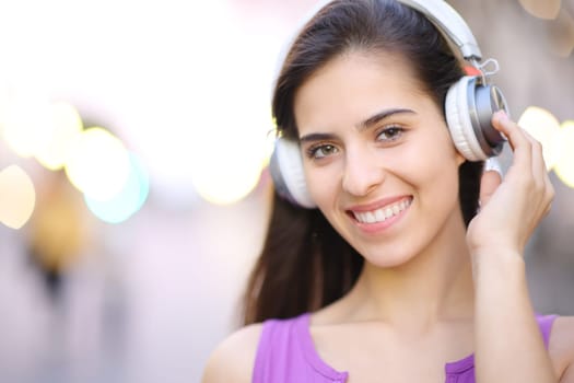 Happy woman with headphones looks at camera in the street