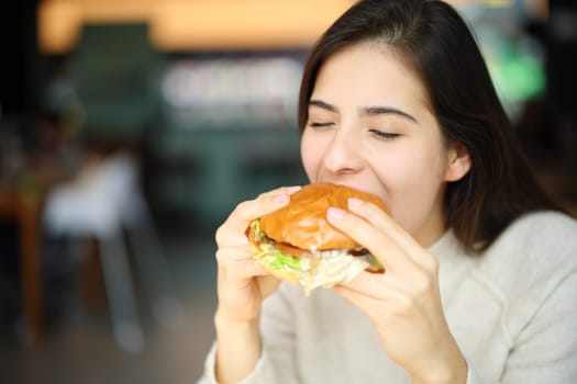 Happy woman eating burger in a restaurant
