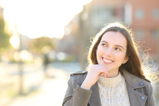 Front view portrait of a happy woman thinking looking at side in the street