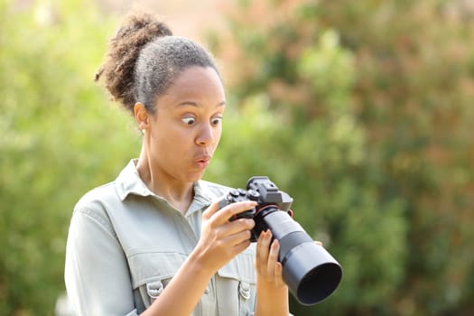 Surprised black photographer checking photos on mirrorless camera in a park