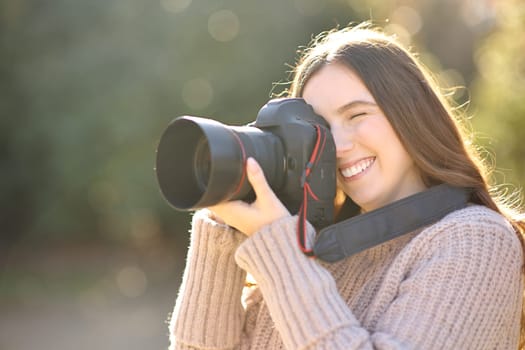 Happy woman taking photos in winter with professional camera in a park