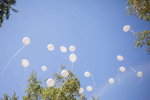 White balls in sky. Balloons fly through air. Details of holiday. Flying in sky.