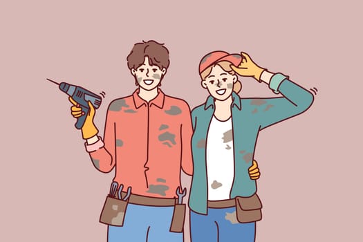 Married couple is engaged in repair or construction with own hands and poses in dirty clothes with screwdriver. Happy man and woman smiling and looking at camera while building own house