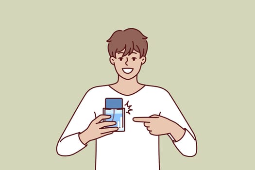 Man pointing finger at perfume bottle recommending to buy cologne or antiperspirant with cool scent. Happy guy employee of perfume shop holding sample of deodorant that protects against bad smell