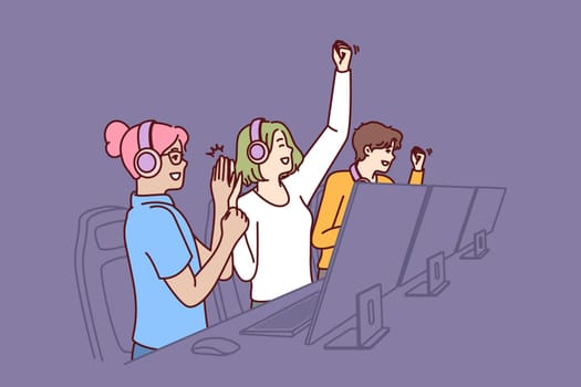 Team of delighted esports players participating in gamer competition in online multiplayer game or MMORPG. Teenage boys and girls sit at table with computers and celebrate victory in tournament