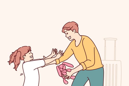 Little girl runs to father who returned from long business trip with gift and wants to hug daughter. Man with toy hare in hand stands near suitcase and rejoices when he sees daughter running towards