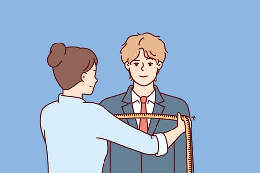 Woman tailor measures shoulders of man in centimeters to make formal suit to individual measurements. Guy at reception at tailor making handmade clothes according to individual sketches