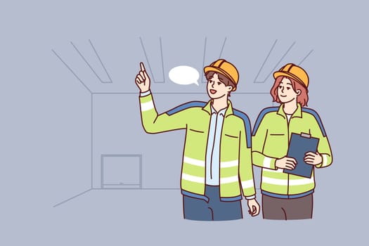Two industrial room engineers discussing production process and how to repair equipment. Man and woman engineers in construction uniforms and safety helmets hold meetings in unfinished building