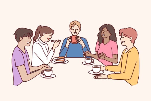 Group of multiethnic colleagues drink coffee sitting at table during break and laugh telling funny jokes. Happy people in casual wear relaxing enjoying socializing and meeting with school friends