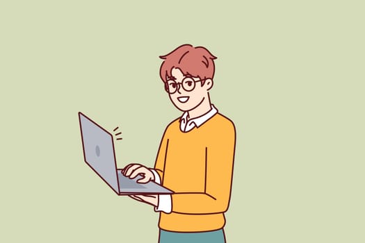 Smart little boy with open laptop for preparing homework assigned from school stands and looks at camera. Schoolboy in casual wear holding laptop using internet and learning software development