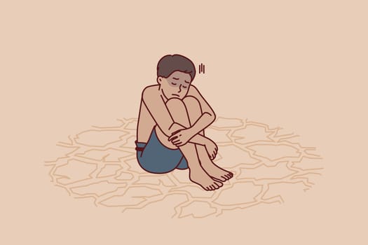 Sad boy feeling thirsty sits on dry ground after global climate change and pollution of ecological environment. Child suffers from lack of drinking water or drought that has destroyed rivers and lakes
