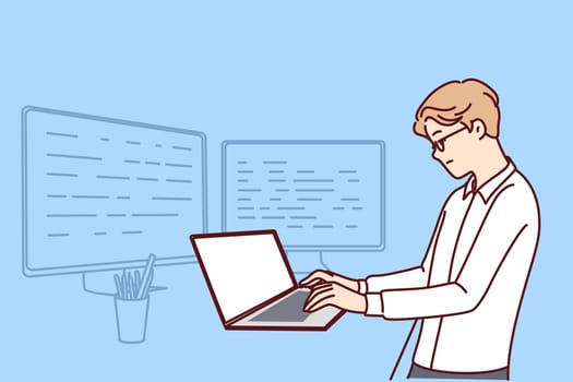 Man software developer is standing at table with laptop and monitors creating server applications. Dispatcher guy works as it analyst using software to monitor load on company computer systems.