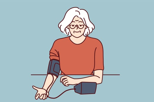Elderly woman uses tonometer to measure blood pressure and check for symptoms of hypertension. Gray-haired grandmother independently measures blood pressure, taking care of own health