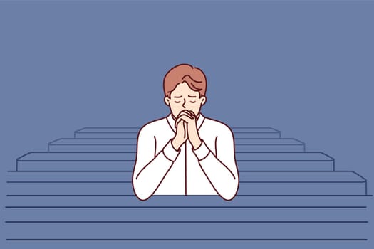 Christian man sits and prays in catholic church, turning to god to confess or ask for help. Believing guy in church and prays to feel psychological relief or observe religious ritual
